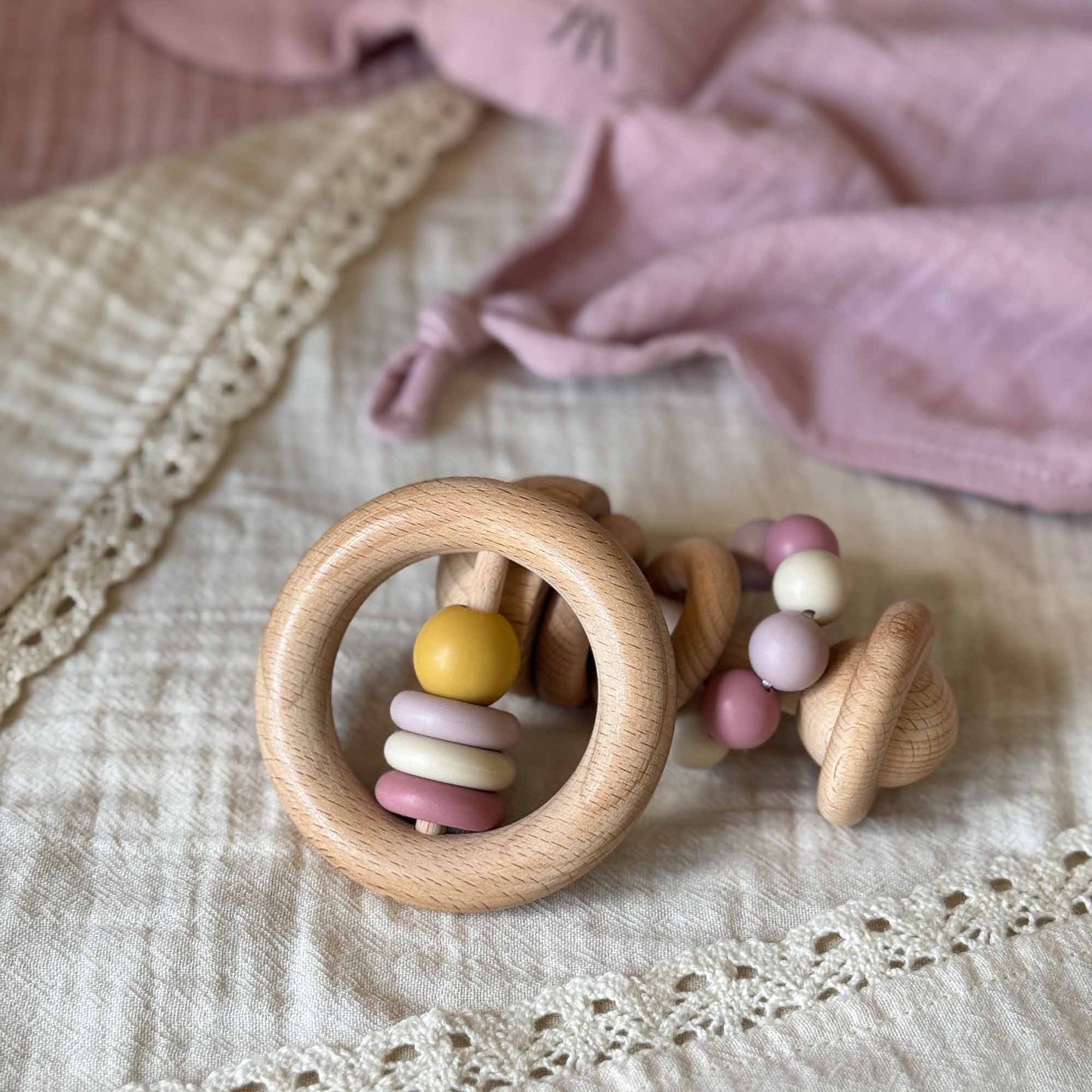 A wooden baby rattle ringrangle rosa with natural finish and pastel yellow lavender pink beads