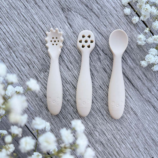 Set med tre beige silikon nybegynnerskjeer med dekorative perforerte hoder og preget logo