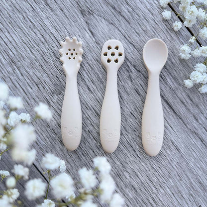 Set med tre beige silikon nybegynnerskjeer med dekorative perforerte hoder og preget logo