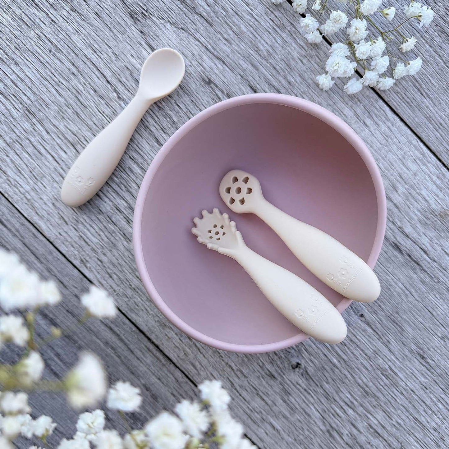 Pastel rosa silikonbolle med to beige nybegynnerskjeer med blomsterhode for babyspising inni