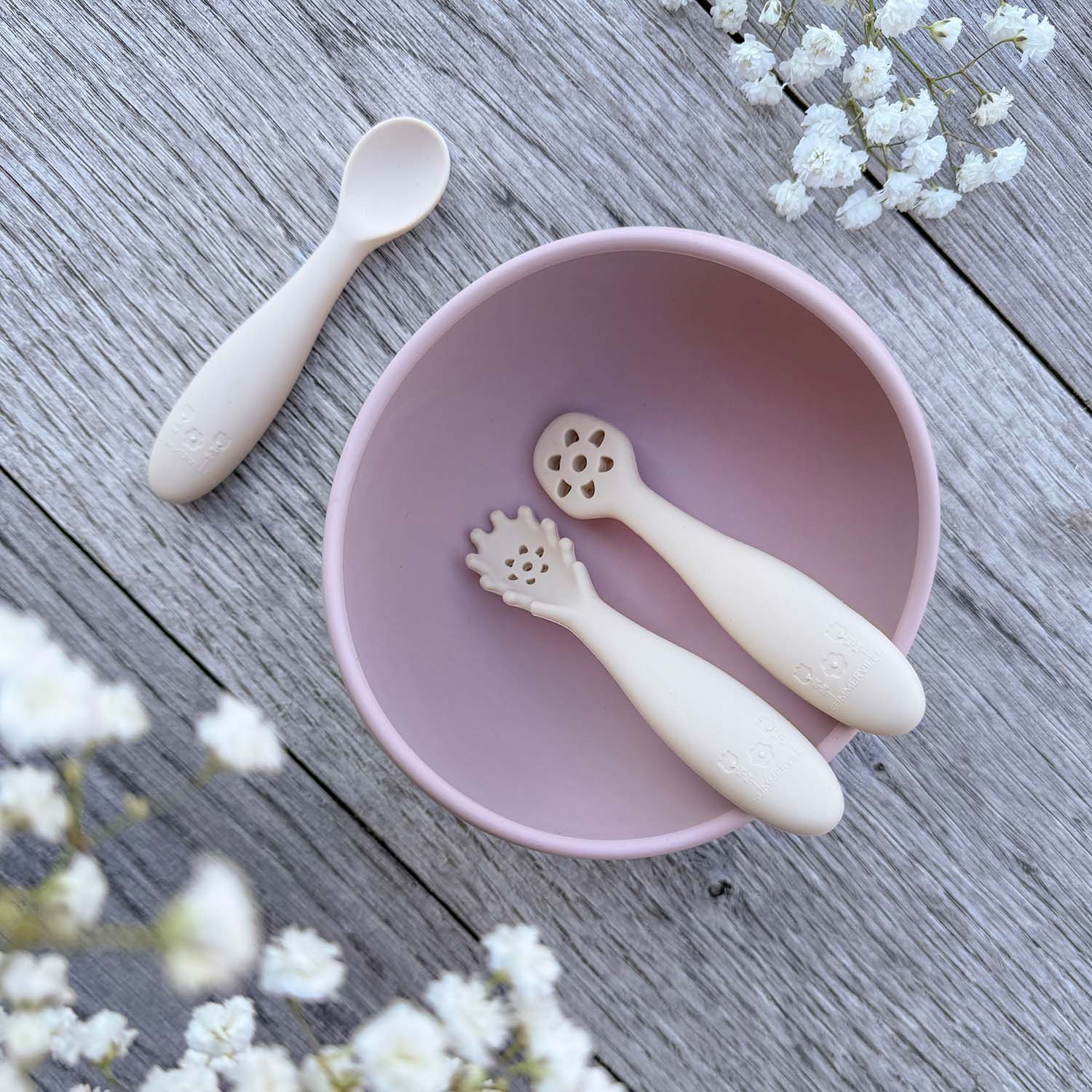 Pastel rosa silikonbolle med to beige nybegynnerskjeer med blomsterhode for babyspising inni