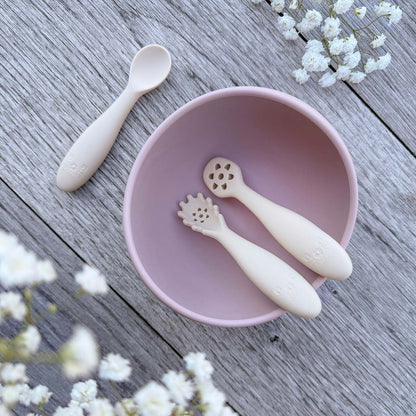 Pastel rosa silikonbolle med to beige nybegynnerskjeer med blomsterhode for babyspising inni
