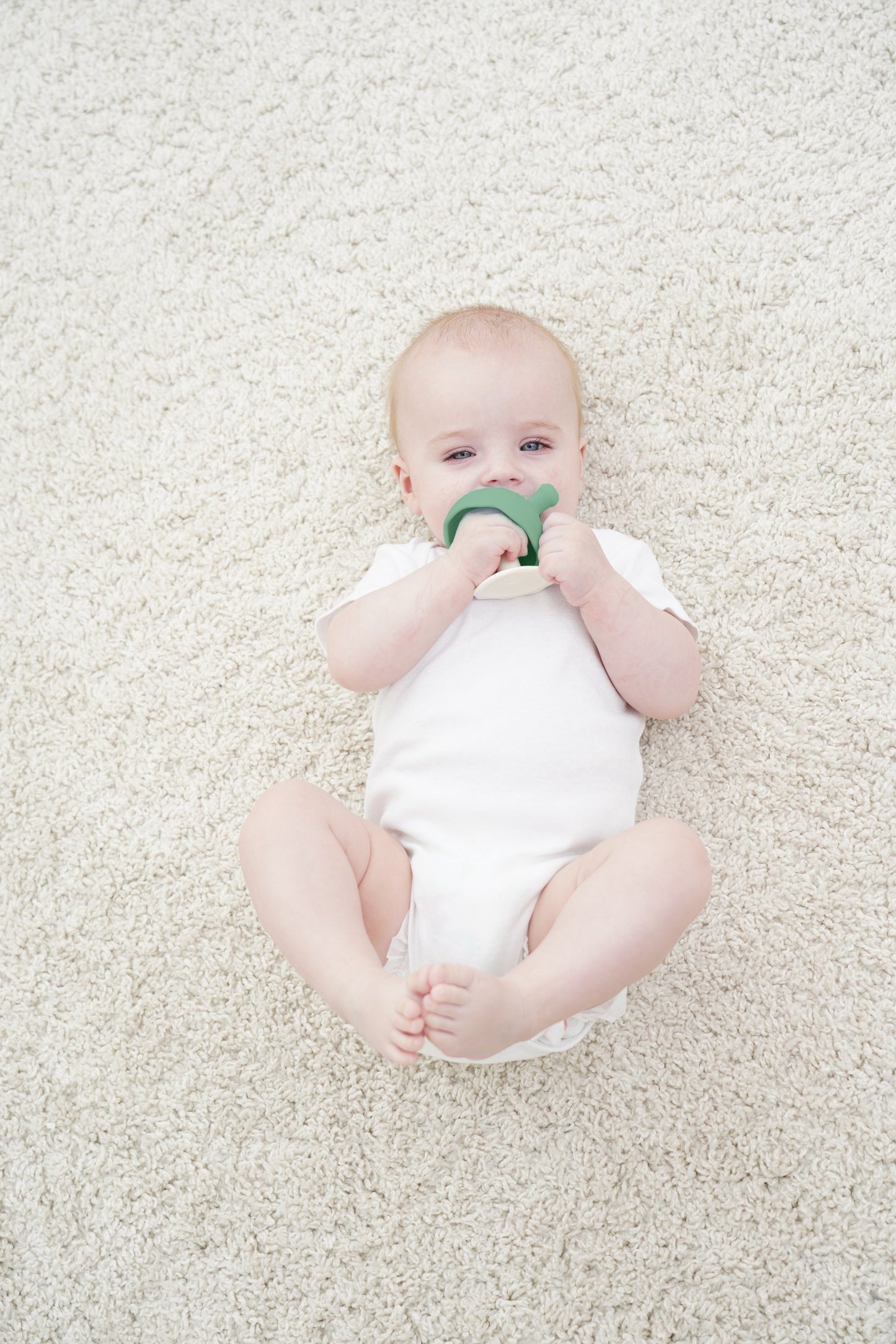 En baby i hvit heldrakt holder en grønnbeige silikon tannutstyr sopp eukalyptus som tåler oppvaskmaskin