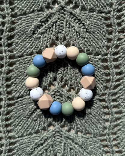 Pastellfarget håndlaget bitering i bpa fri silikon med runde og geometriske perler i blått, grønt, beige og hvitt som lindrer ømme gommer