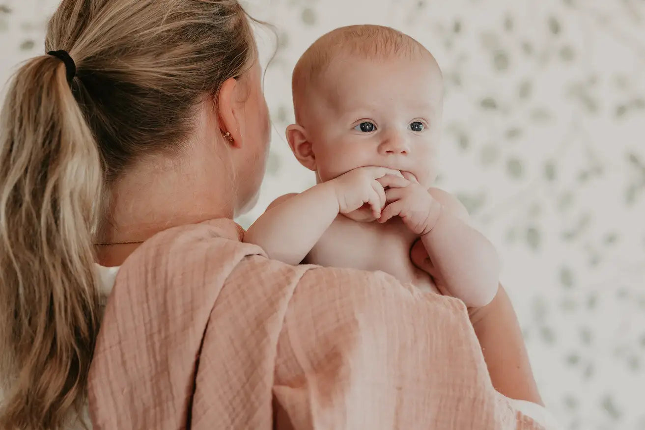 Et mykt, ferskenfarget musselintrekk omfavner en baby med en delikat, naturlig stofftekstur.