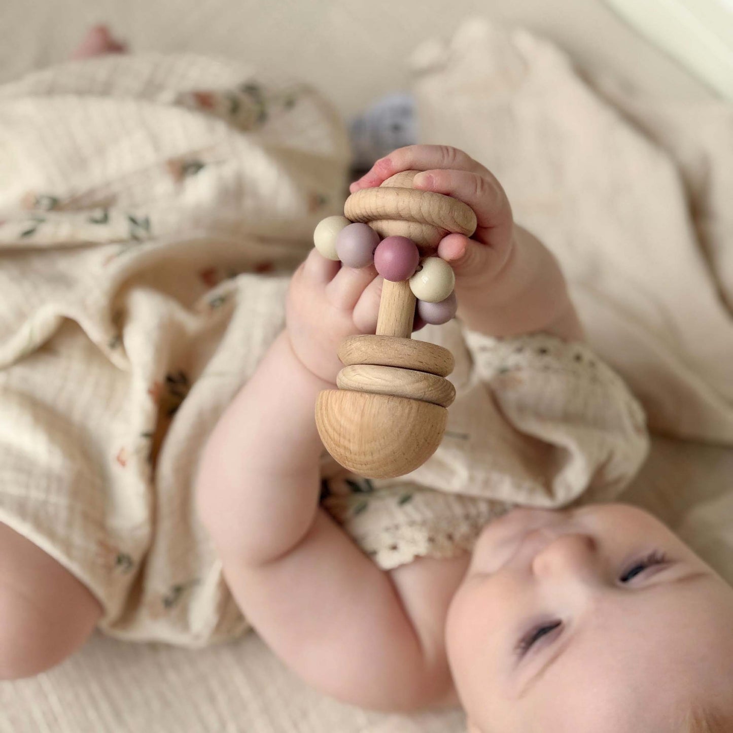 A baby holds a rosa trerangle teething rattle with pastel beads made of fsc sertifisert ubehandlet bøketre