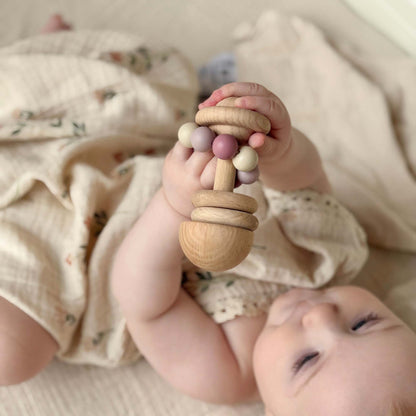 A baby holds a rosa trerangle teething rattle with pastel beads made of fsc sertifisert ubehandlet bøketre