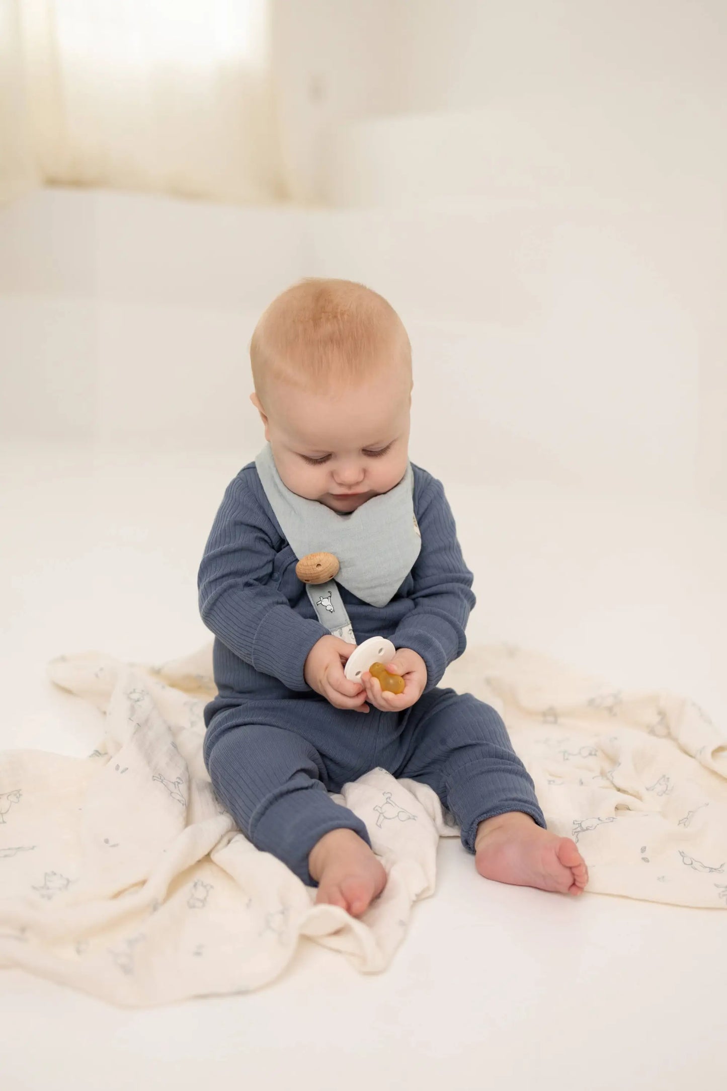 Baby i marineblå ribbestrikket body med lys grå smekke med trekknapper holder smokken med praktisk klips i økologisk bomull