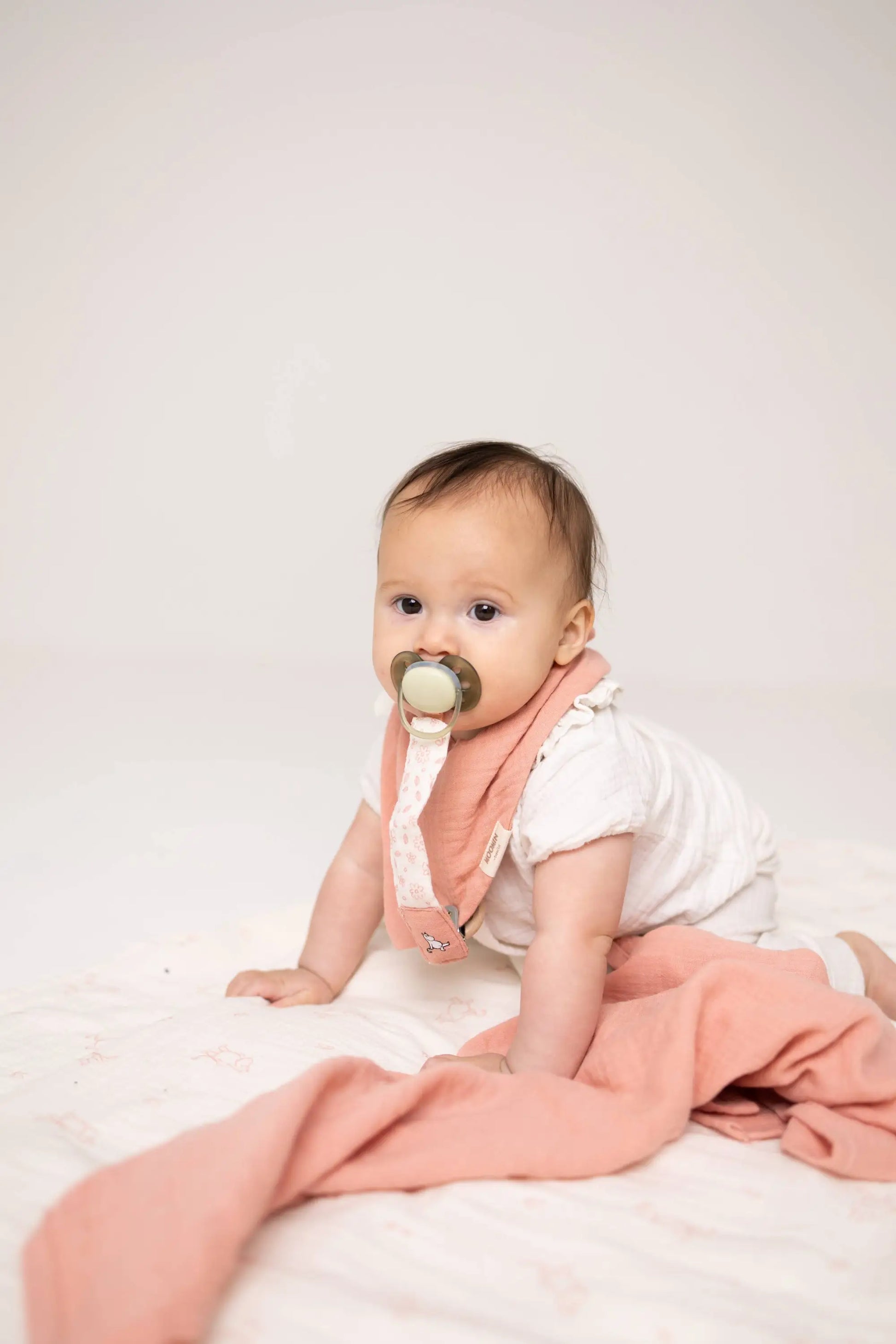 Soft peach-colored moomin smokkelenke rosa baby bib with delicate polka dots in økologisk bomull and praktisk klips holder smokken