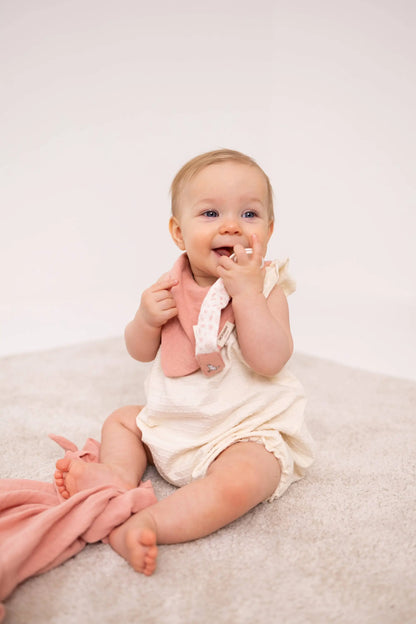 En baby i offwhite økologisk bomull romper med rosa rundeprikket bib og moomin smokkelenke med praktisk klips