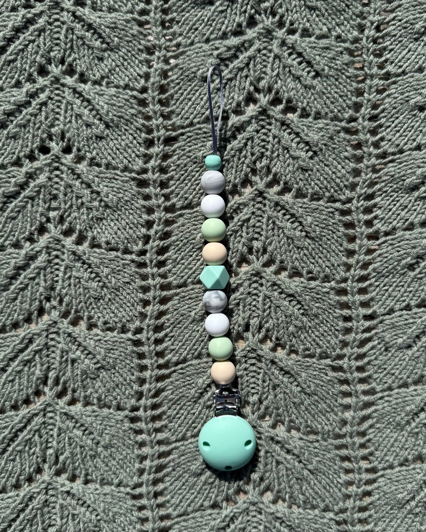 A håndlaget smokkelenke i bpa fri silikon med mintgrønn festeklemme og pastellfargede geometriske perler