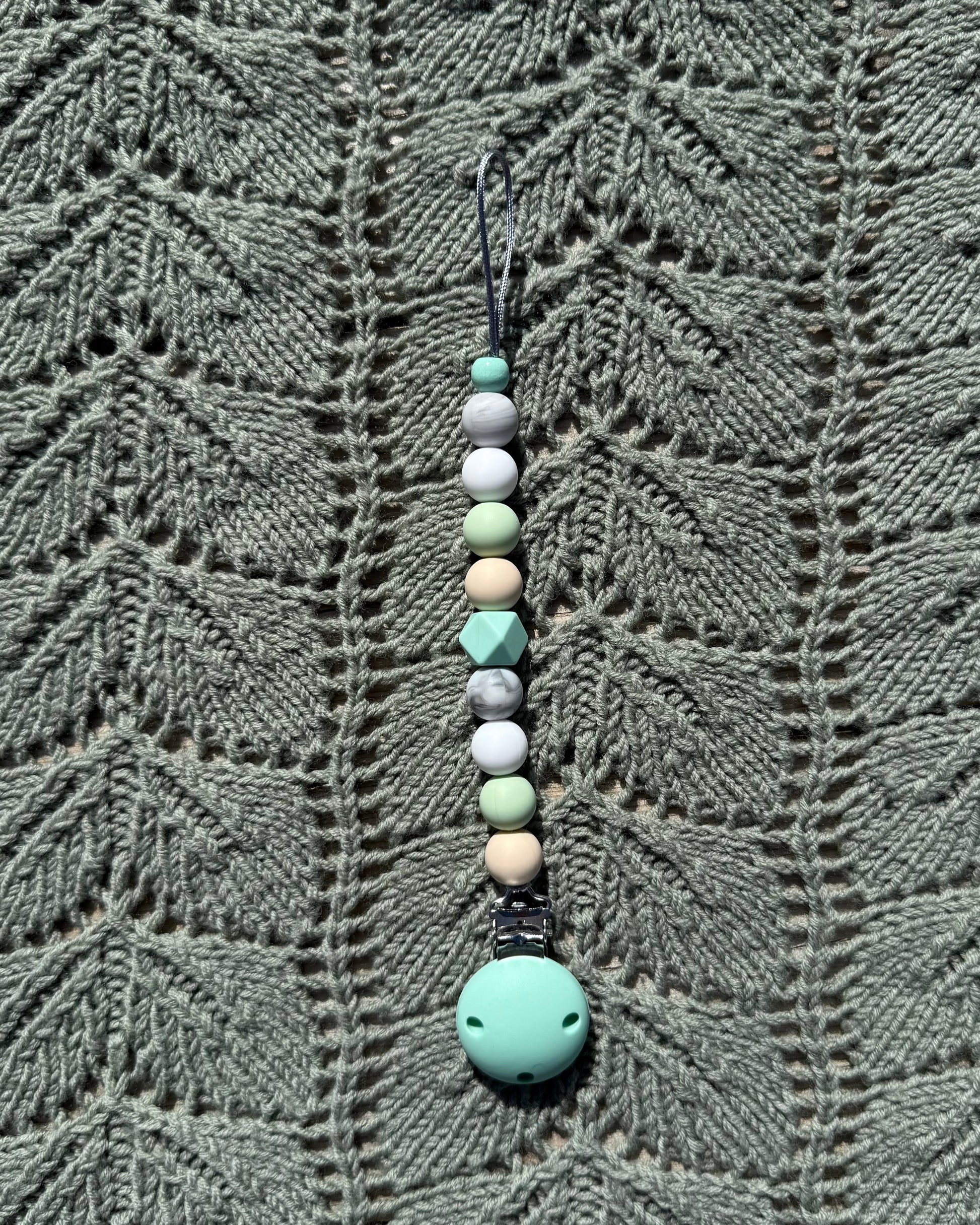 A håndlaget smokkelenke i bpa fri silikon med mintgrønn festeklemme og pastellfargede geometriske perler