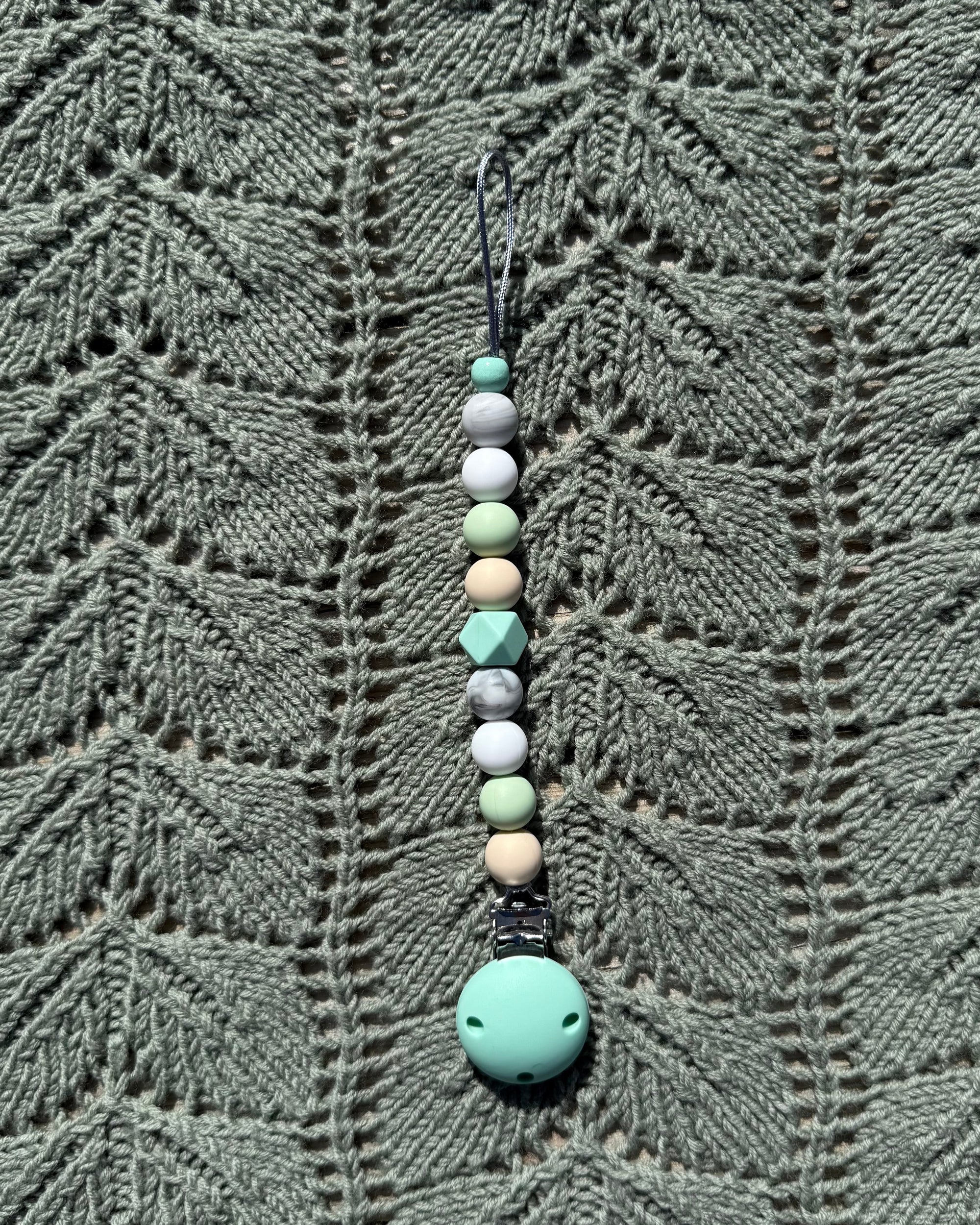 A håndlaget smokkelenke i bpa fri silikon med mintgrønn festeklemme og pastellfargede geometriske perler